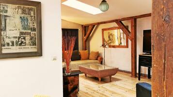 Ein gemütliches Zimmer mit Holzboden, einem gewebten Hocker, einer Couch und einem gerahmten Bild an der Wand.