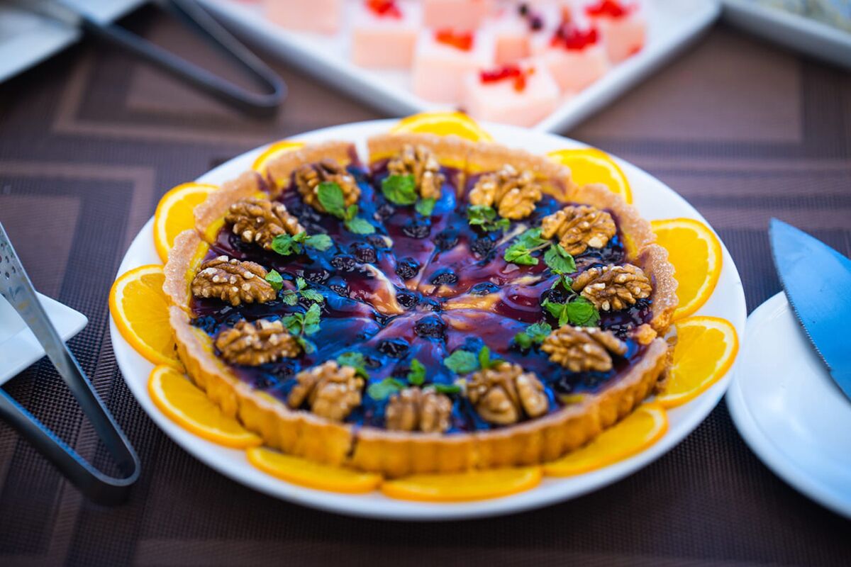A dessert with a fruit topping, garnished with nuts and mint leaves, on a white plate with orange slices around the edge.