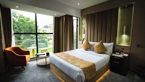 Ein Hotelzimmer mit einem großen Bett, einem Sessel, einem Nachttisch und Blick ins Grüne.