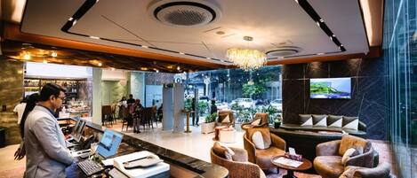 A hotel lobby with a reception desk, seating area, and a large TV screen.