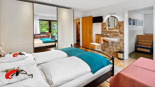 Quarto de hotel moderno com uma cama grande, banheiro com pia e espelho, e vista para o exterior.