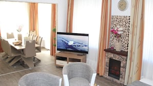 Una sala de estar moderna con televisor de pantalla plana, chimenea y comedor con sillas y mesa.