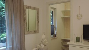 Quarto com cama, cômoda, espelho, um vaso com flores e janela com cortinas.