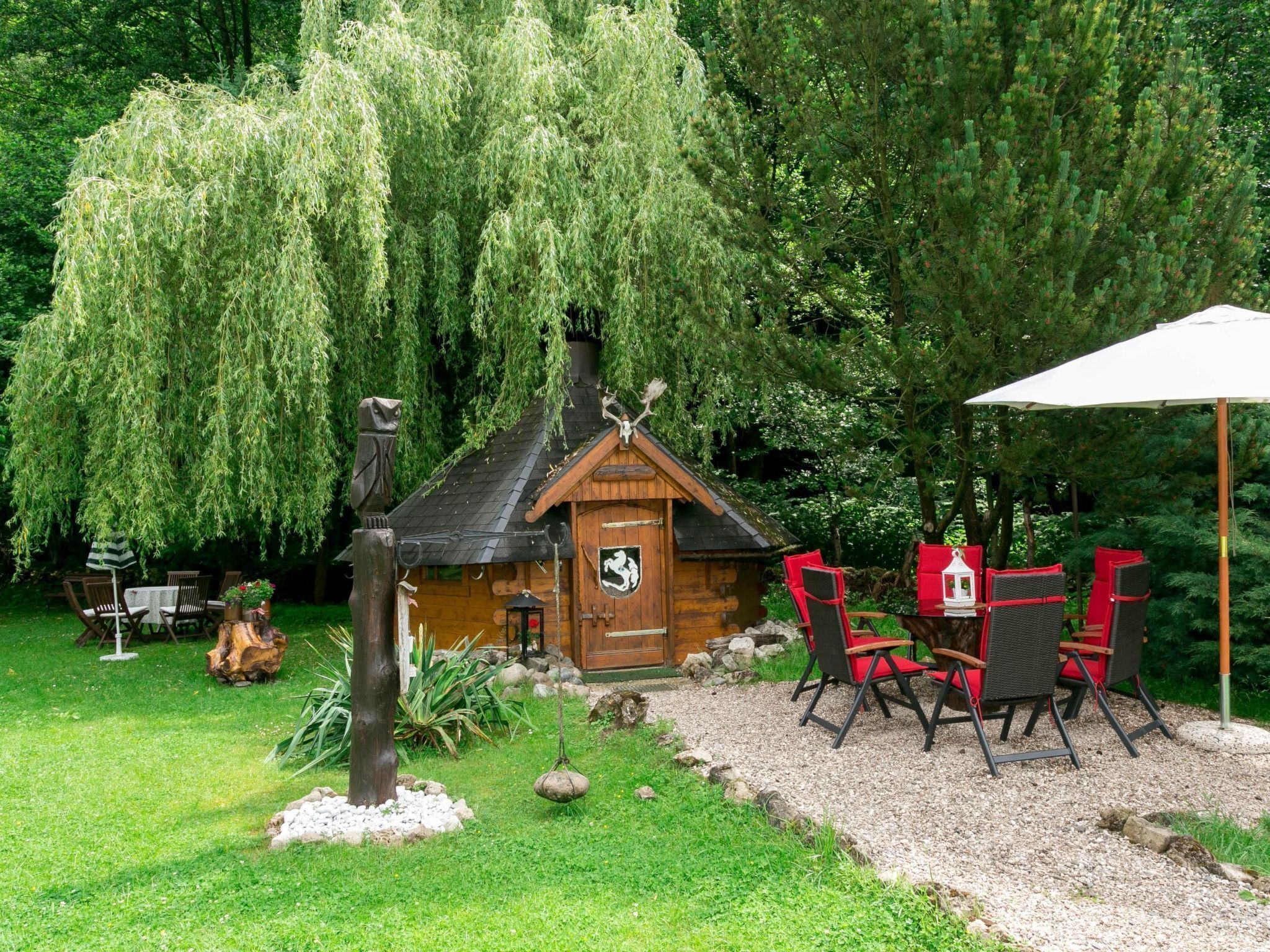 Eine rustikale Holzhütte mit Strohdach, umgeben von üppigem Grün und einem Schotterweg.