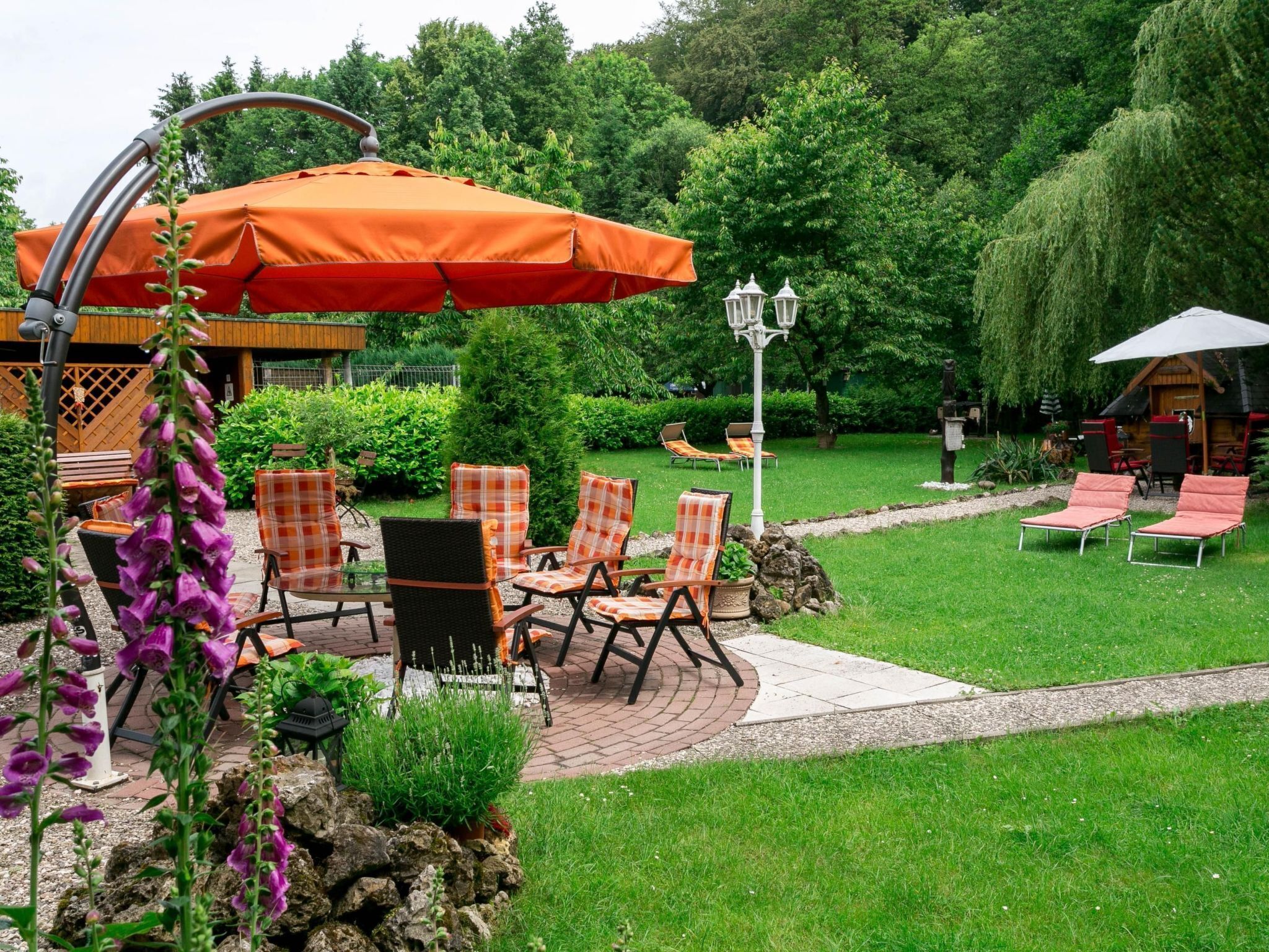 An outdoor patio area with a table and chairs, surrounded by greenery and a small wooden structure.