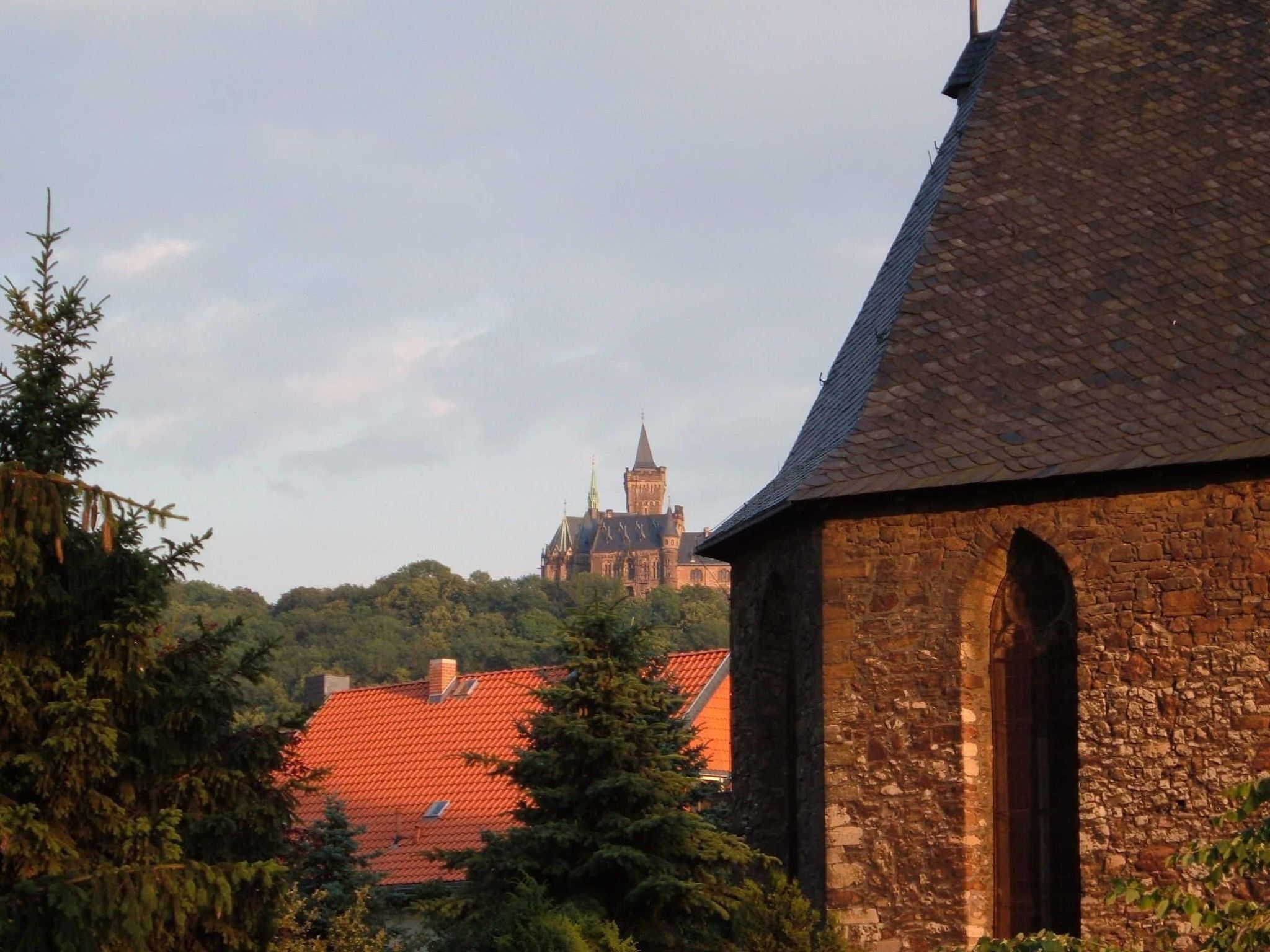 A stone building with a red-tiled roof, surrounded by trees.