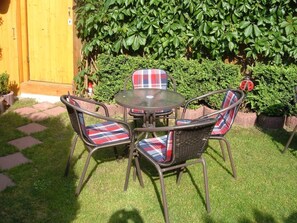 Eine Terrasse mit einem runden Tisch und vier Korbstühlen mit karierten Kissen.