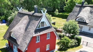 Ett rött hus med ett halmtak, omgivet av grönska och en asfalterad uppfart.