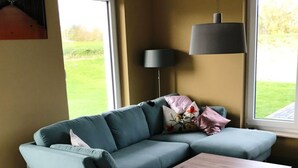 Un salon moderne avec un canapé d’angle, un petit pouf, une table basse en bois et un lampadaire.