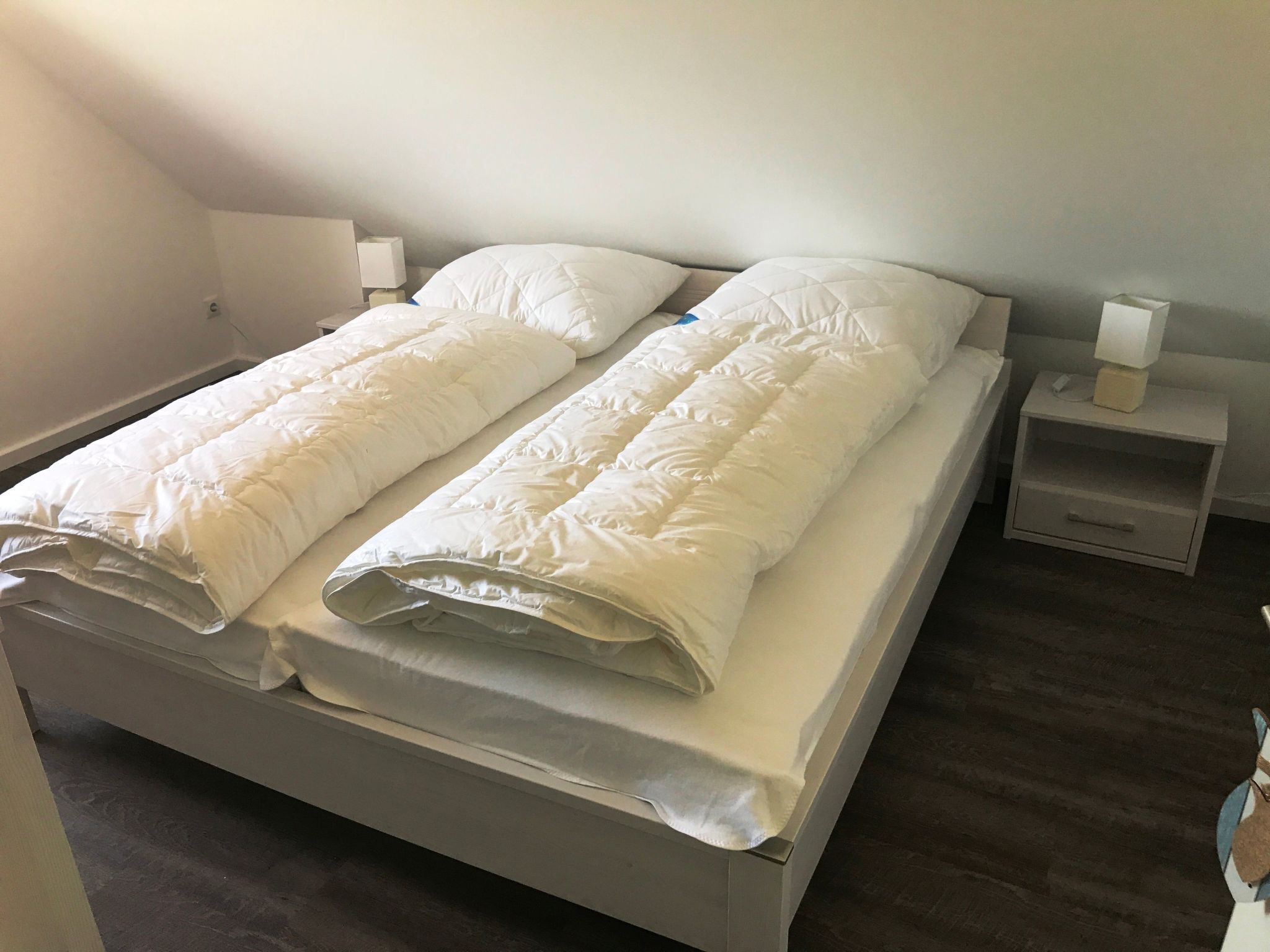 Een tweepersoonsbed met witte lakens, twee nachtkastjes en een nachtkastje met een lamp.