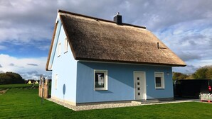 Une maison de plain-pied avec un toit de chaume, une porte blanche et une petite fenêtre à l’avant.