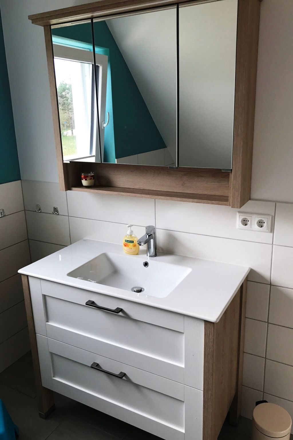 Une salle de bain avec un lavabo blanc, un miroir et un meuble en bois.