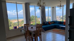A spacious room with a dining area, a sofa set, and large windows offering a view of the sea and landscape. - Wohnung Panoramablick by Interhome (Tanger)