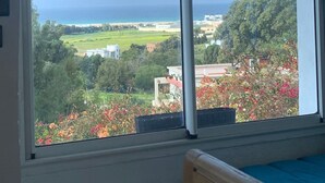 A room with a large window overlooking a landscape with greenery and a distant view of the sea. - Wohnung Panoramablick by Interhome (Tanger)