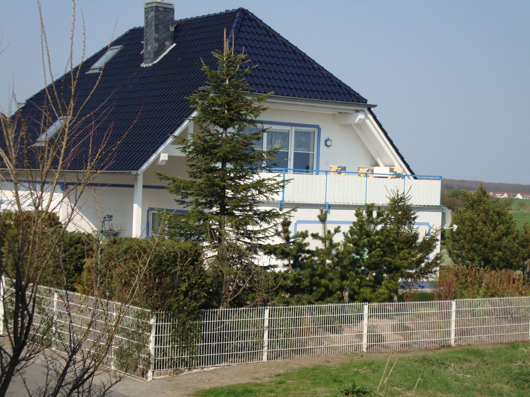 Een huis met twee verdiepingen, met een donkerblauwe dak, witte muren en een blauw raamkozijn.