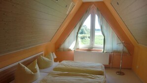 A bedroom with a sloped ceiling, a bed with pillows, a radiator, and a window with curtains. - Nette Wohnung mit Garten, Grill und Pool by Interhome (Beetzsee)