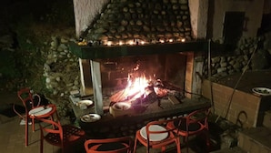 Un espace barbecue extérieur avec une cheminée en pierre, deux chaises rouges et une table.