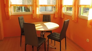 A dining area with a round table and four chairs, large windows with curtains, and orange walls. - mit Pool by Interhome (Beetzsee)