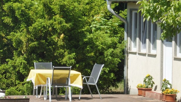 An outdoor patio with a table and chairs, surrounded by lush greenery and a building with a white facade. - mit Pool by Interhome (Beetzsee)