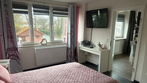 Een slaapkamer met een bed, een bureau, een televisie en uitzicht op buiten.