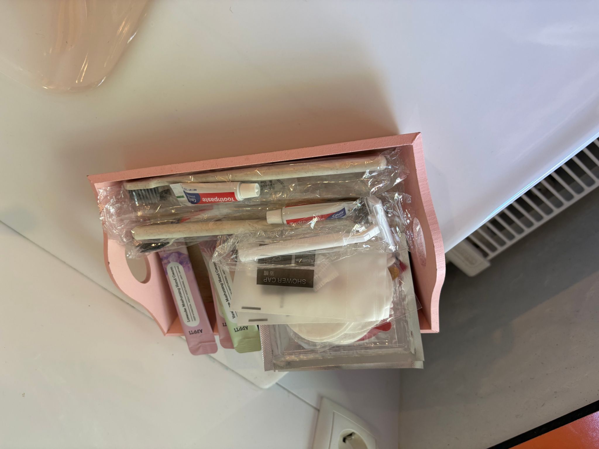 Una scatola rosa contenente diversi oggetti, tra cui un tubetto di dentifricio, un flacone di collutorio e un paio di forbici.