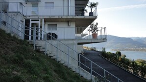 Um edifício com vários andares e uma escadaria que leva a uma varanda com vista para a água e montanhas.