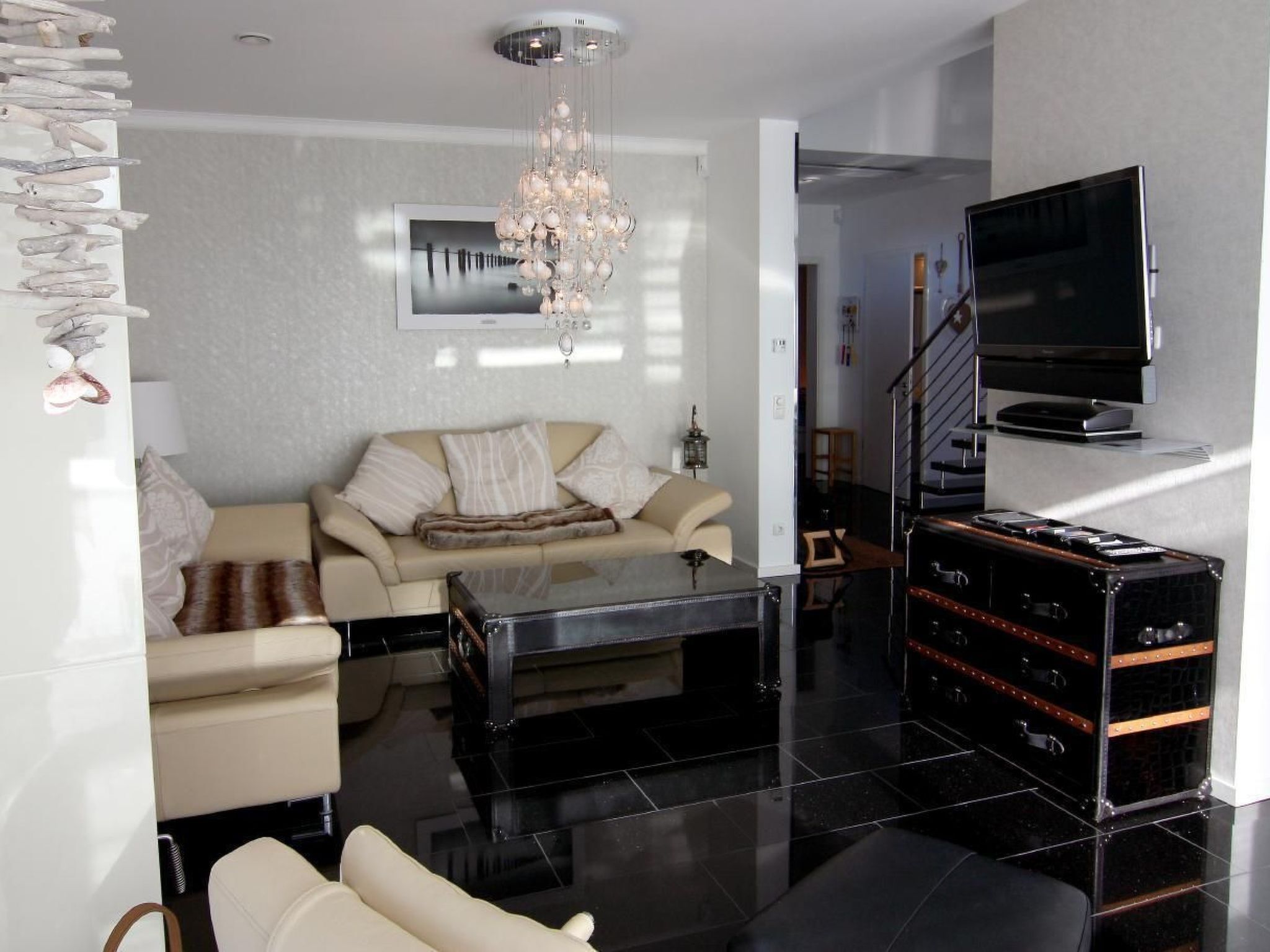 Una sala de estar moderna con un sofá, una mesa de centro, un televisor montado en la pared y una escalera que conduce a otro nivel.