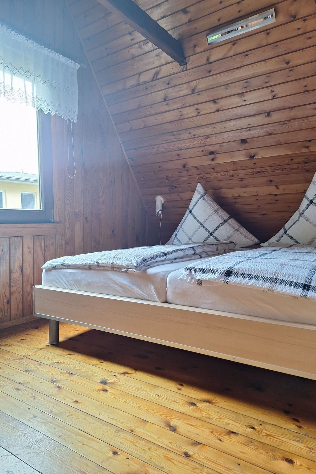 A wooden cabin room with a bed, a window, and a ceiling vent.