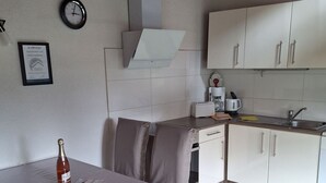 Eine kompakte Küche mit weißen Schränken, einem eingebauten Ofen und einem Spülbecken. Ein Esstisch steht bereit, mit einer Weinflasche und einer Speisekarte.