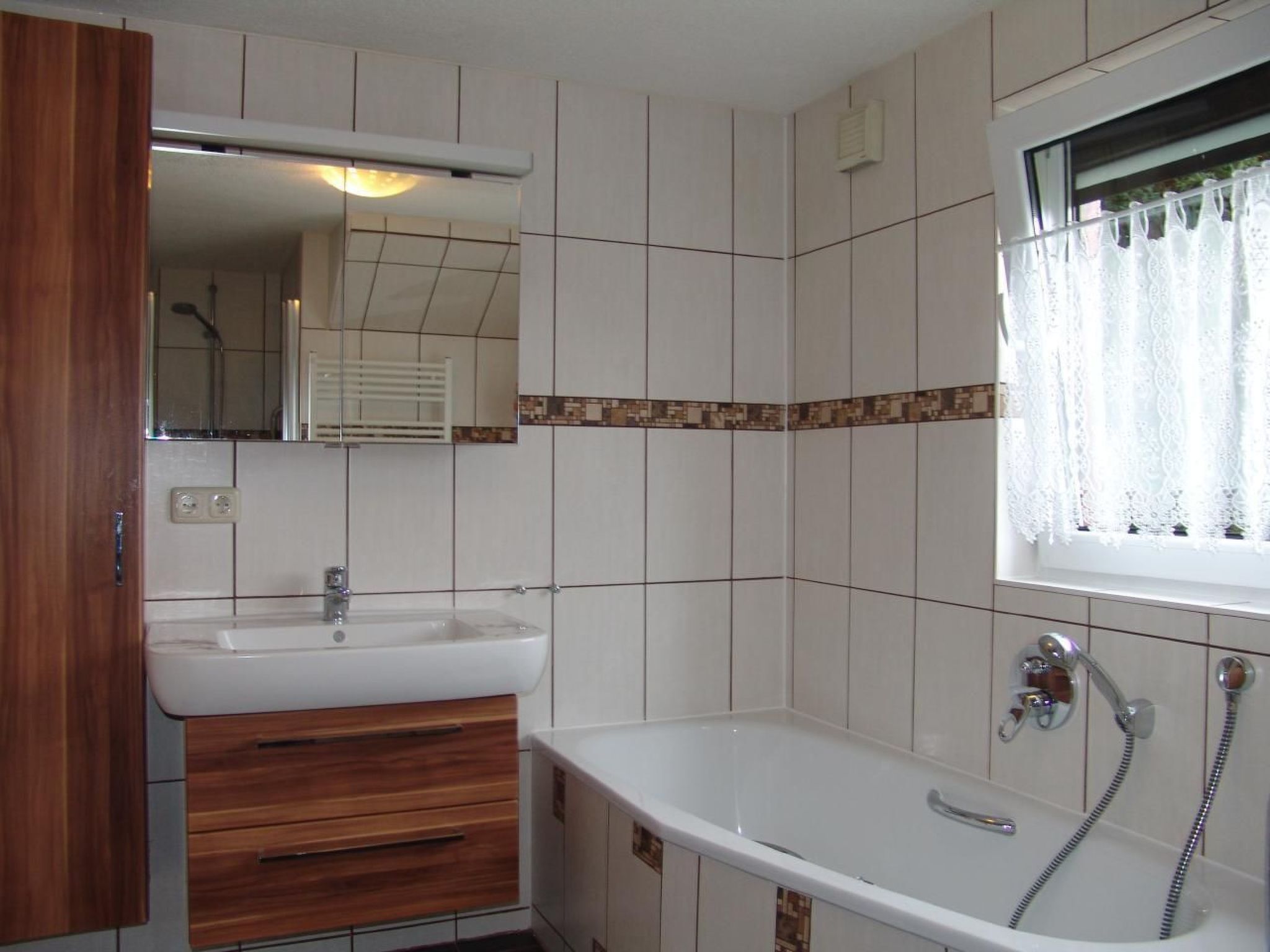 Ein Badezimmer mit Waschbecken, Holzschrank und Badewanne mit Duschbrause.