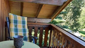 A covered outdoor seating area with a table and chairs, a wooden railing, and a view of greenery. - in Bayerisch Eisenstein mit Garten by Interhome (Bayerisch Eisenstein)