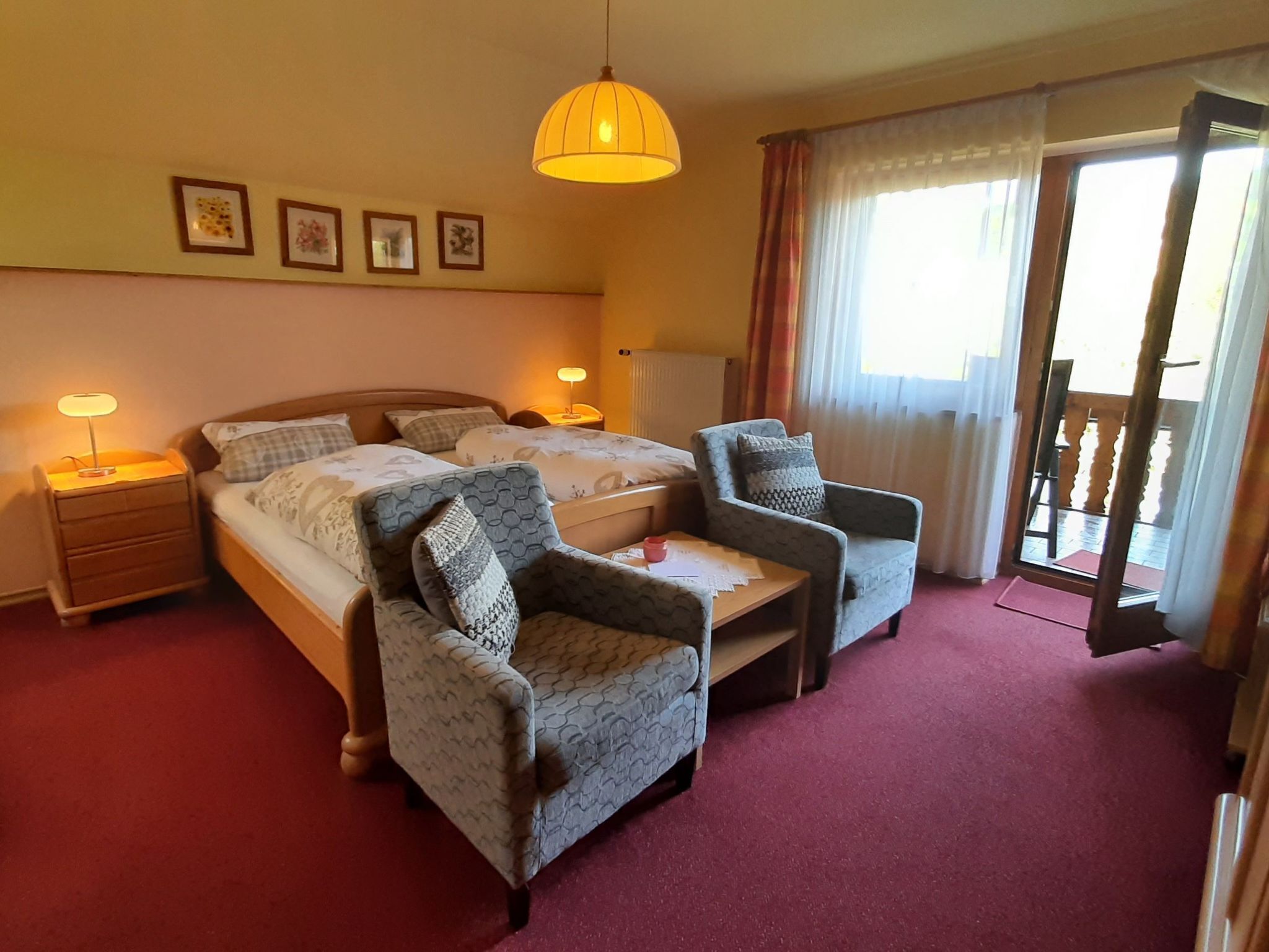 Ein Hotelzimmer mit zwei Betten, einer Sitzecke mit Sesseln, einem Schreibtisch und einem Balkon mit Vorhängen.