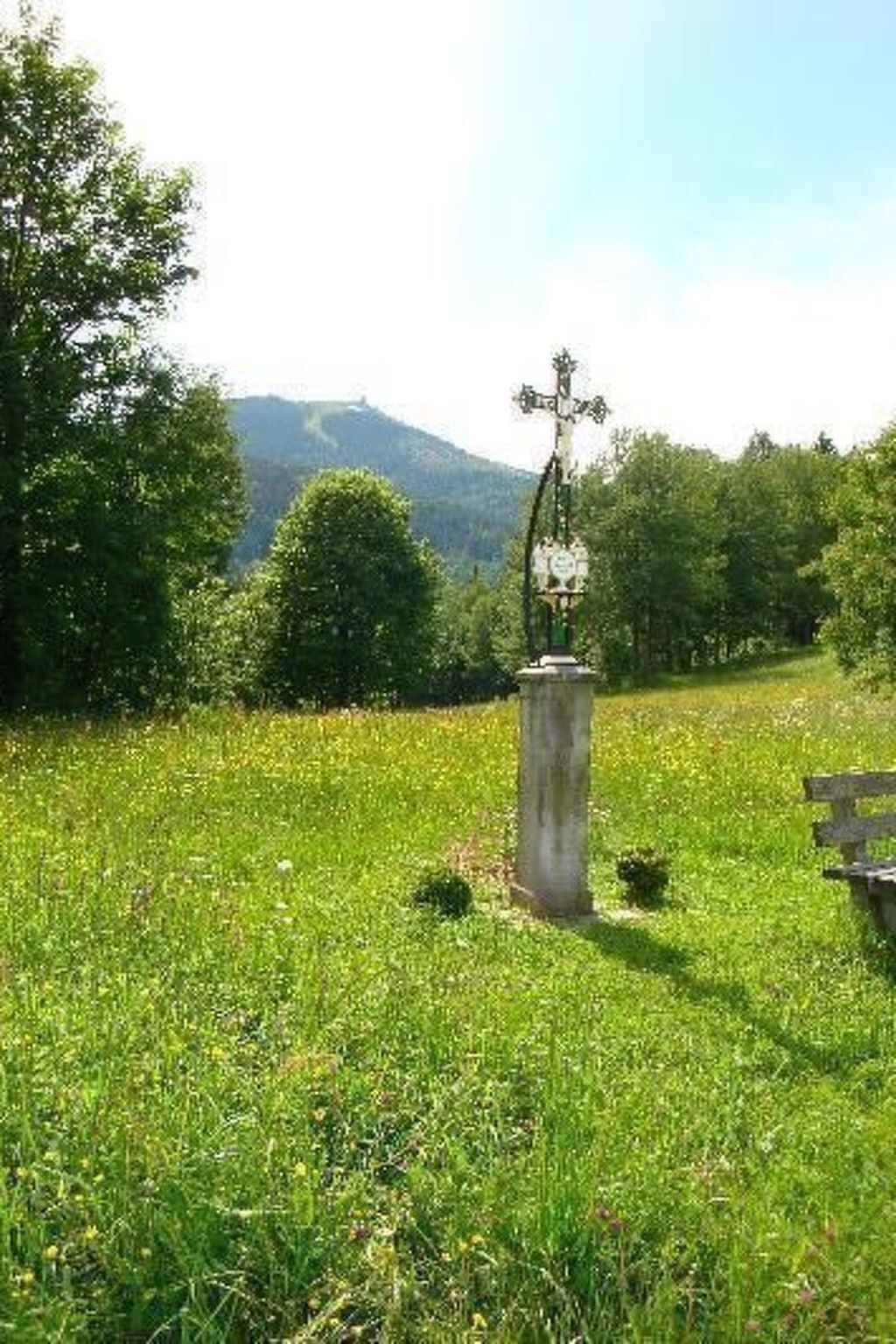 Ein grasbewachsenes Feld mit einem Kreuzdenkmal und einer Bank.