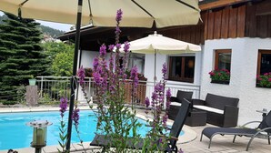 A poolside area with a lounge chair, a large umbrella, and a wooden house in the background. - in Bayerisch Eisenstein mit Garten by Interhome (Bayerisch Eisenstein)