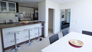 Une cuisine moderne dotée d’un îlot central, de tabourets de bar et d’un coin repas avec une table et des chaises blanches.