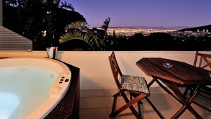 Un bain à remous avec vue sur la ville, une table et des chaises en bois, et un espace patio agrémenté de palmiers.