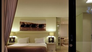 Une chambre moderne avec un grand lit, une table de chevet, une œuvre d’art accrochée au mur et une porte coulissante donnant sur une salle de bain.