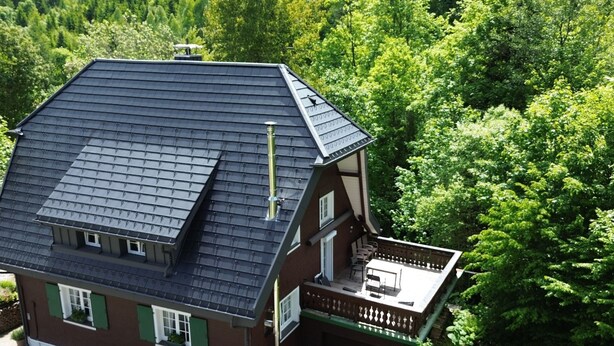 Une maison à deux étages avec un toit sombre, un balcon doté de sièges pour l’extérieur et un jardin.