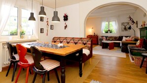 Un salon chaleureux avec une table à manger en bois, des chaises rouges et noires, un canapé et une cheminée.