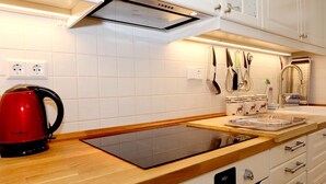 Une cuisine moderne avec des meubles blancs, un plan de travail en bois, une bouilloire rouge, une horloge numérique et divers ustensiles de cuisine.