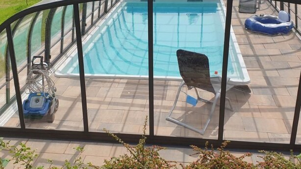 Une piscine couverte avec une structure en verre, une chaise longue et un anneau gonflable bleu.