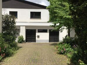 A two-story house with a paved driveway and a garden with various plants and flowers. - Eifelhaus4you by Interhome (Schleiden)
