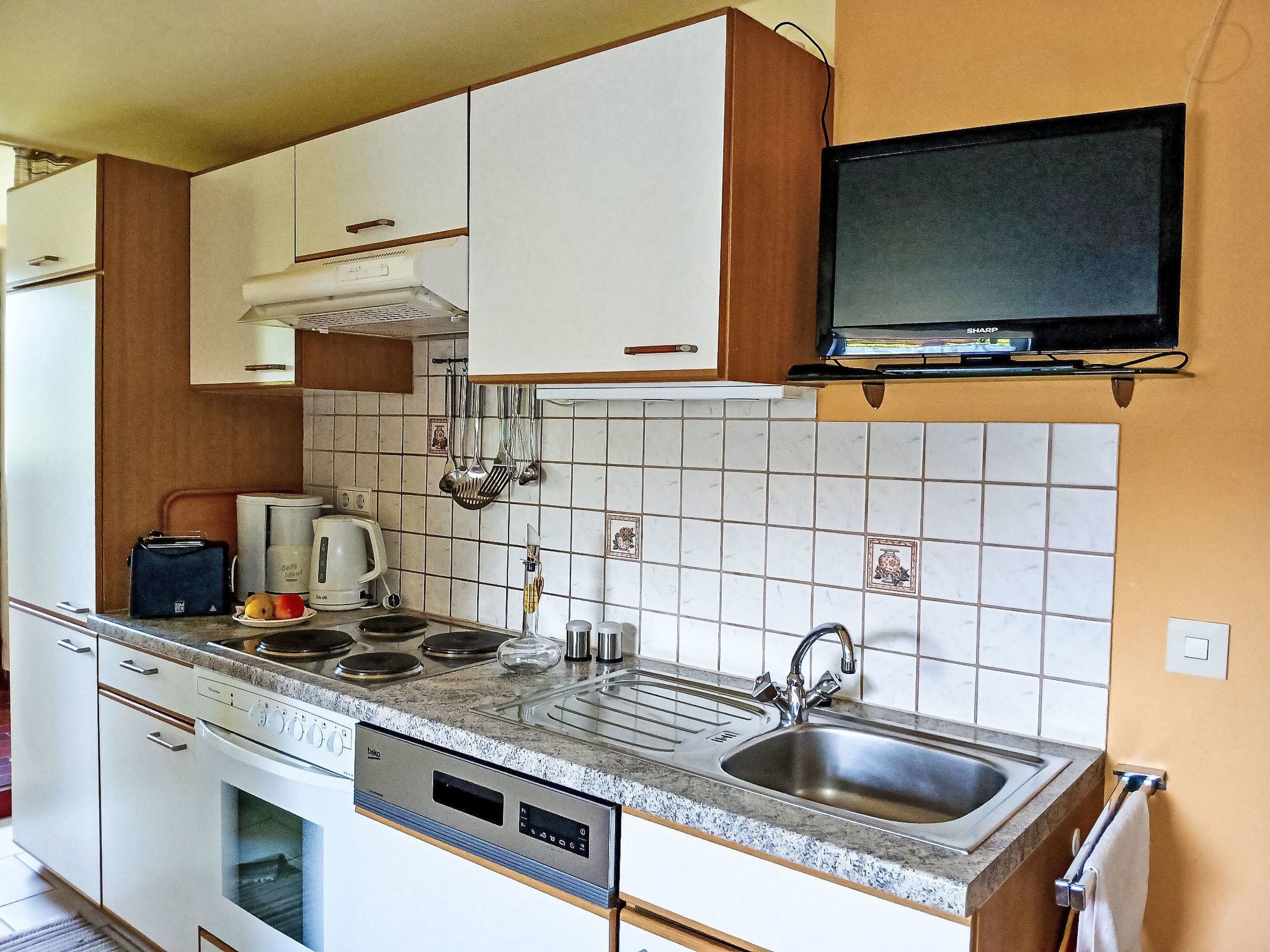 A compact kitchen with white cabinets, a built-in oven, a microwave, a coffee maker, and a sink.