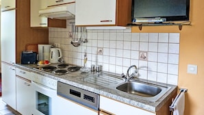 Cocina compacta con armarios blancos, horno empotrado, microondas, cafetera y lavamanos.