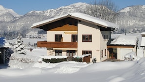 Un chalet de dos pisos con balcón de madera, rodeado de montañas nevadas.