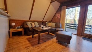 A cozy room with a wooden ceiling, a sofa, a table with a vase of flowers, and a window with a view of trees. - Marie 125 by Interhome (Bad Arolsen)