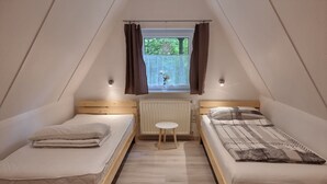 A small, triangular attic bedroom with two wooden beds, a small table, and a window with curtains. - Marie 125 by Interhome (Bad Arolsen)