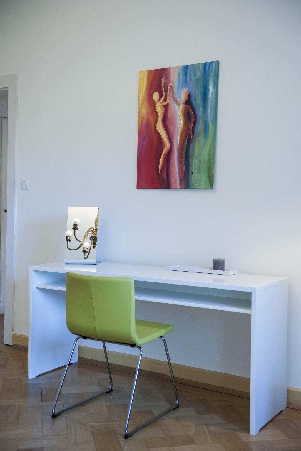 Un espacio de oficina moderno con un escritorio blanco, una silla verde y un cuadro abstracto colorido en la pared.