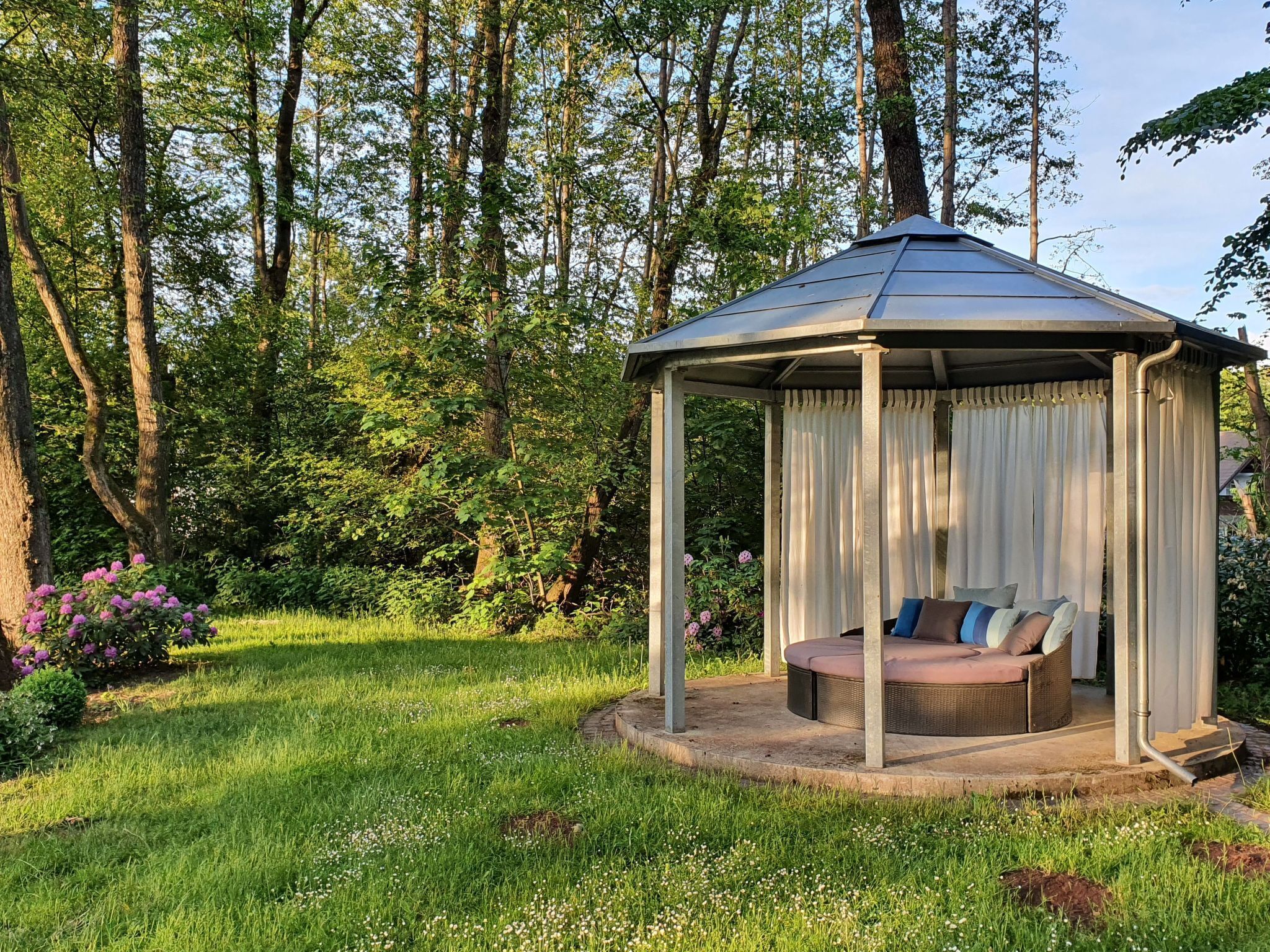 Ein Kiosk mit überdachtem Sitzbereich, umgeben von üppiger Vegetation und Bäumen.