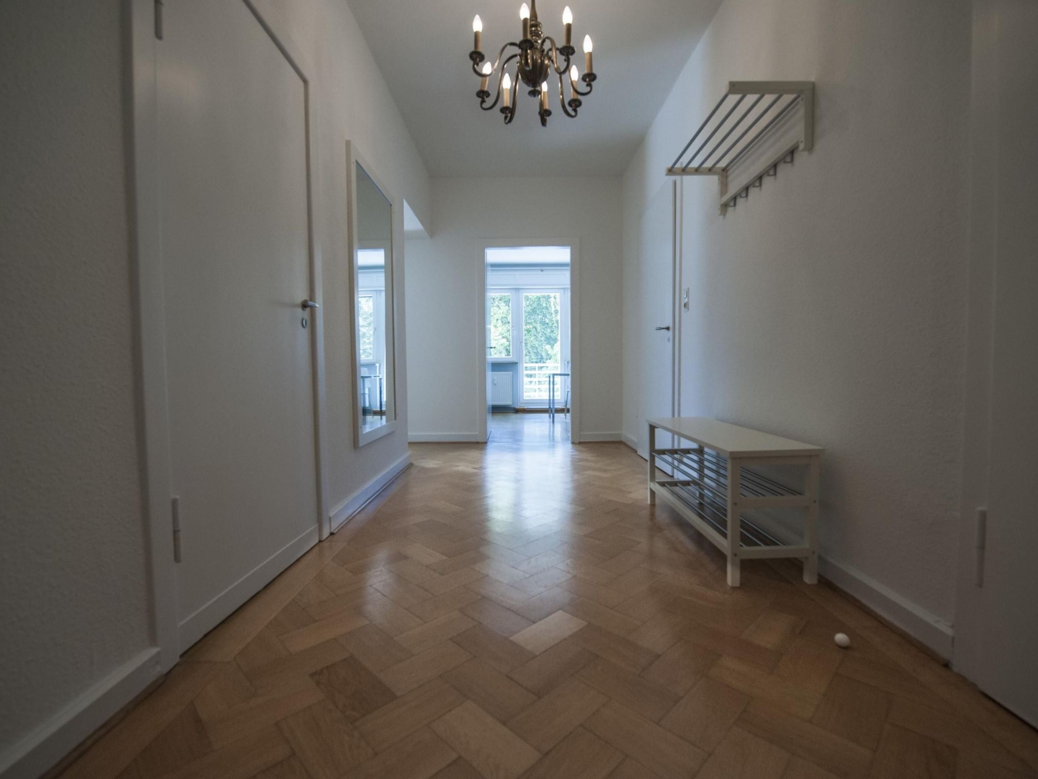 Ein Flur mit Holzboden, weißen Wänden, einer Chandelierleuchtre und einer Bank.